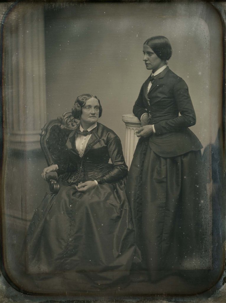 A black and white photograph of Charlotte Cushman, seated with her lover, Matilda Hays, standing at her side.